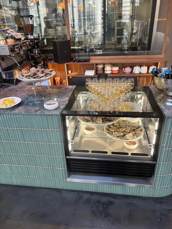 Oyster bar display case with fresh oysters and champagne glasses at an upscale seafood restaurant with teal tile counter.